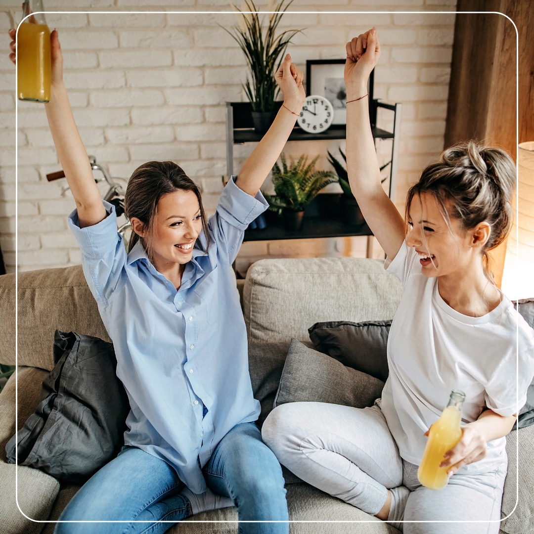 Zwei Frauen auf dem Sofa mit Getränken – Sinnbild für moderne, flexible Stromtarife, die Energie bezahlbar und transparent machen.