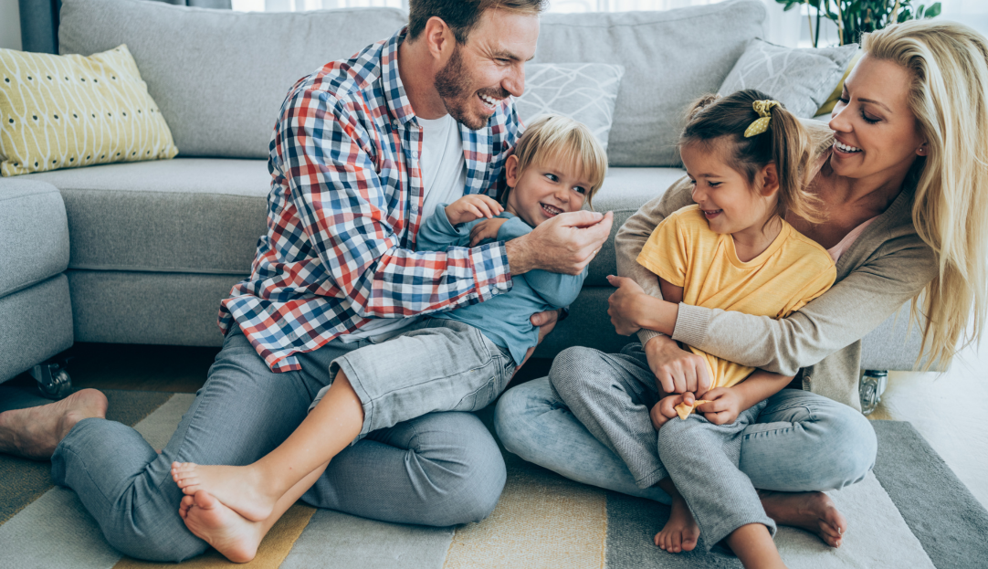 Eine Familie mit Vater, Mutter und zwei Kindern sitzt glücklich zu Hause – steht für zuverlässige, nachhaltige Energieversorgung und ein sorgenfreies Zuhause mit fairen Stromtarifen.